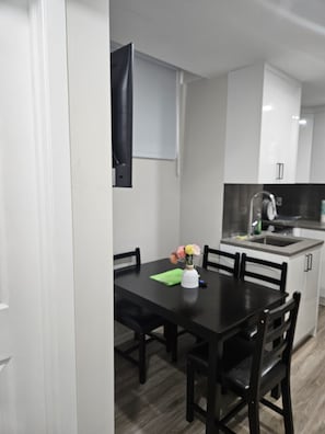 A compact kitchen with white cabinets, a black countertop, and a sink. There is a dining table with chairs and a vase with flowers. - Lovely 2-bedroom apartment basement in  Airdrie perfect for relaxing stay (Airdrie)