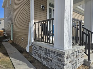 A house with a stone foundation, a porch with a black railing, and a window with a light fixture. - Lovely 2-bedroom apartment basement in  Airdrie perfect for relaxing stay (Airdrie)