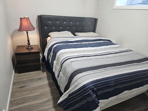 A bed with a dark headboard, a bedside table with a lamp, and a striped bedspread. - Lovely 2-bedroom apartment basement in  Airdrie perfect for relaxing stay (Airdrie)