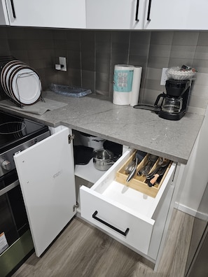A compact kitchen with a built-in refrigerator, a countertop with a coffee maker, and a drawer with utensils. - Lovely 2-bedroom apartment basement in  Airdrie perfect for relaxing stay (Airdrie)