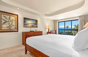 Ein Hotelzimmer mit einem großen Bett, einem Schreibtisch, einem Sessel, einem Fernseher und einem Fenster mit Meerblick.