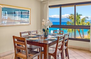 Ein Essbereich mit Tisch für vier Personen, mit Blick auf einen Strand, Palmen und den Ozean.