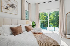 A bedroom with a large bed, a bedside table, a mirror, and a view of the outdoors. - Dallas–McKinney Modern Retreat  5BR • Games • EV Charging (McKinney)