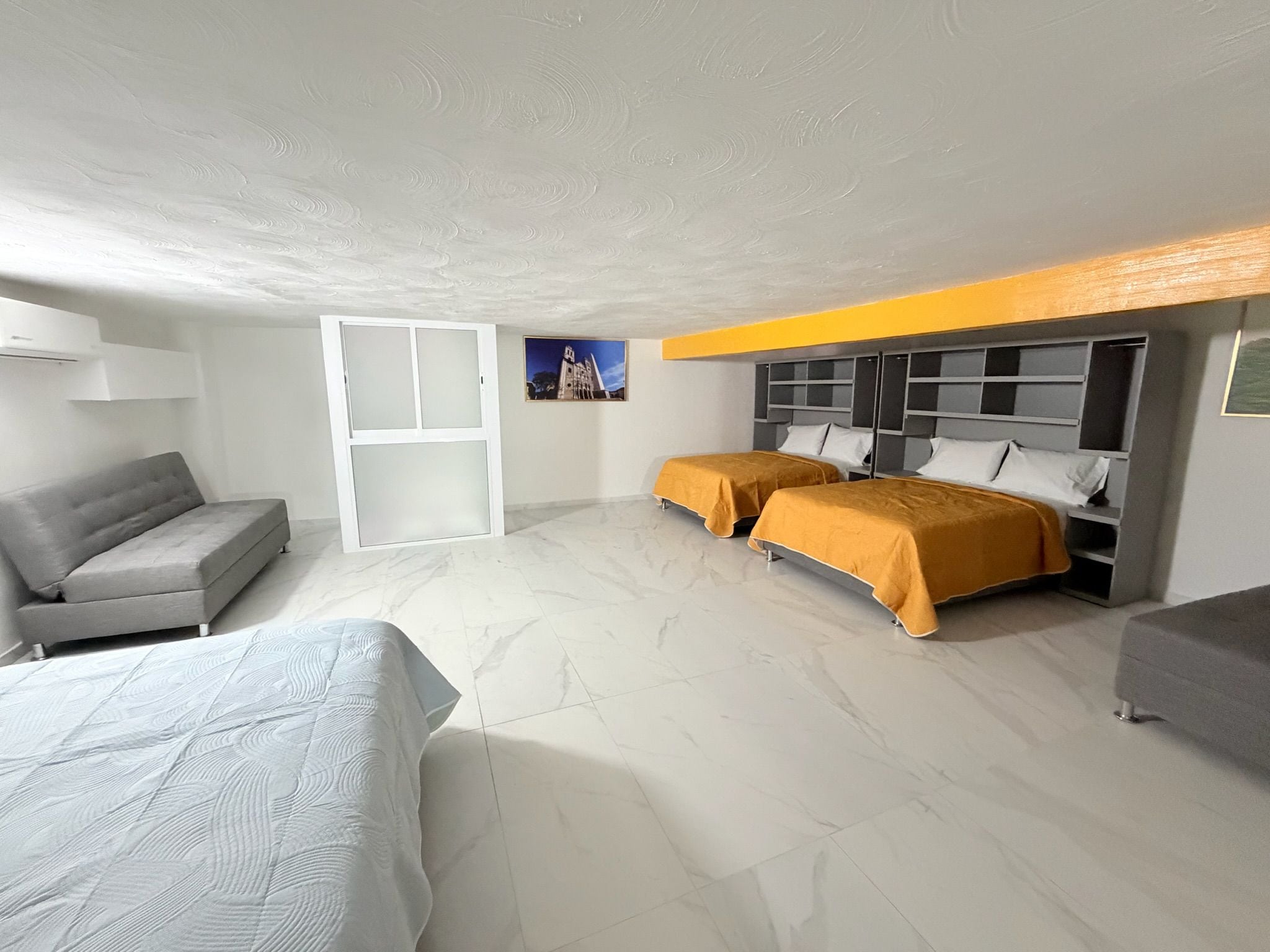 Habitación de hotel con dos camas, un sofá, un ventanal grande y un cuadro en la pared.