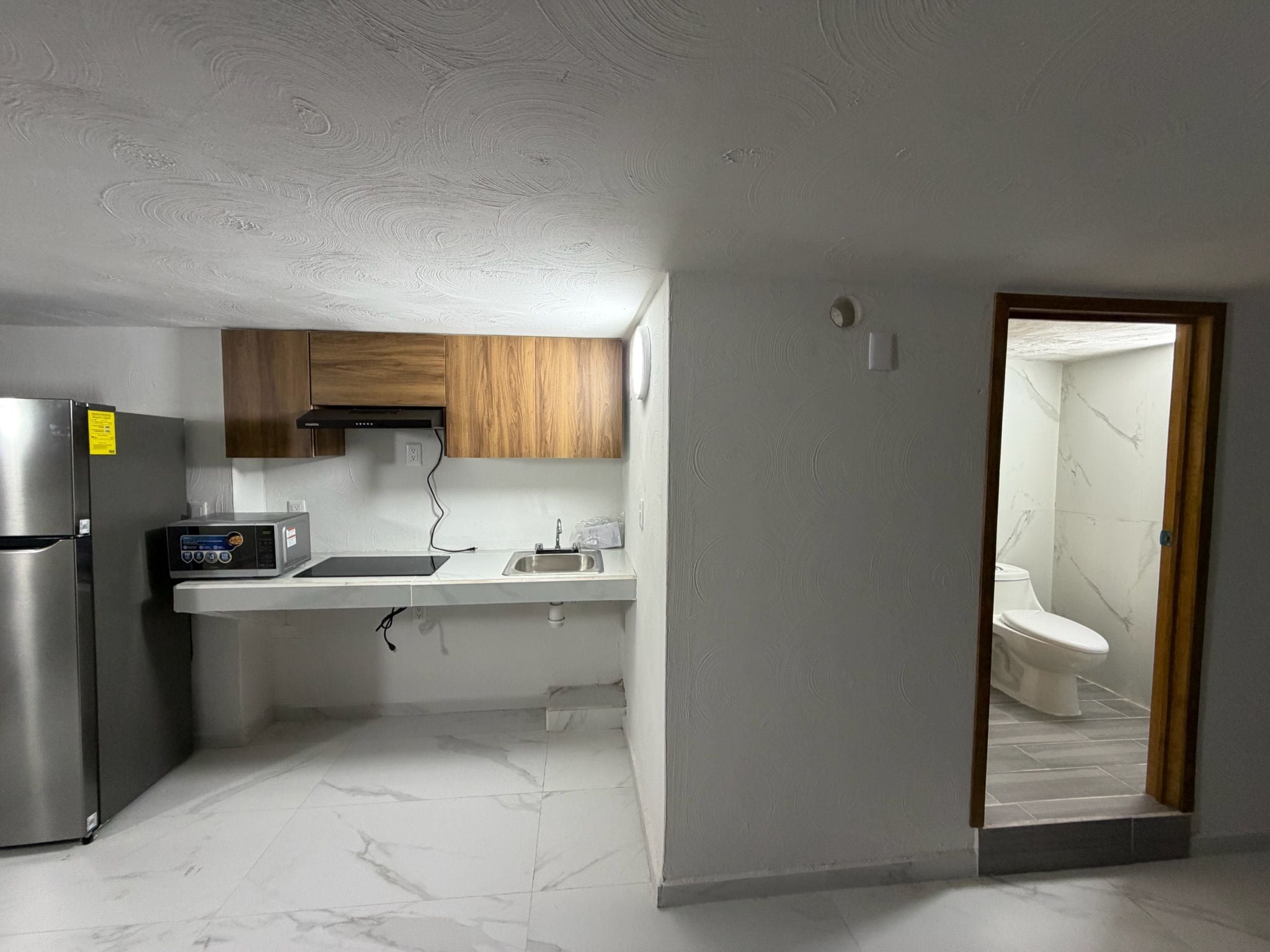 Una cocina compacta con refrigerador empotrado, estufa y armarios de madera.