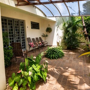 A covered patio area with wicker chairs, a small wall-mounted plant, and a variety of tropical plants.