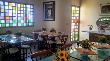 A dining area with glass tables and chairs, a ceiling fan, and a large window with colorful stained glass.