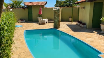 A swimming pool with a stone deck, surrounded by potted plants and a small patio area with a table and chairs.