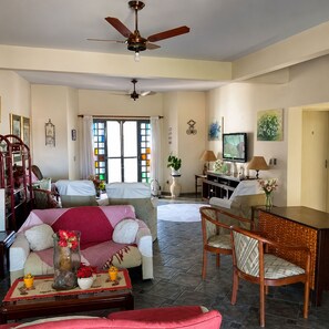 A living room with a sofa, chairs, a coffee table, a TV, and a ceiling fan.