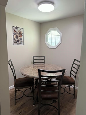 A dining area with a round table, four chairs, a ceiling light, a framed floral artwork, and a window. - The Liberty House / 3 BR • 2 BA / SPIRE • Wineries • Lake Erie (Geneva)