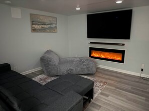 A modern living room with a sectional sofa, a fireplace, and a large TV mounted on the wall.