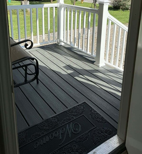 A wooden deck with a white railing, a bench, and a doormat with a monogram.