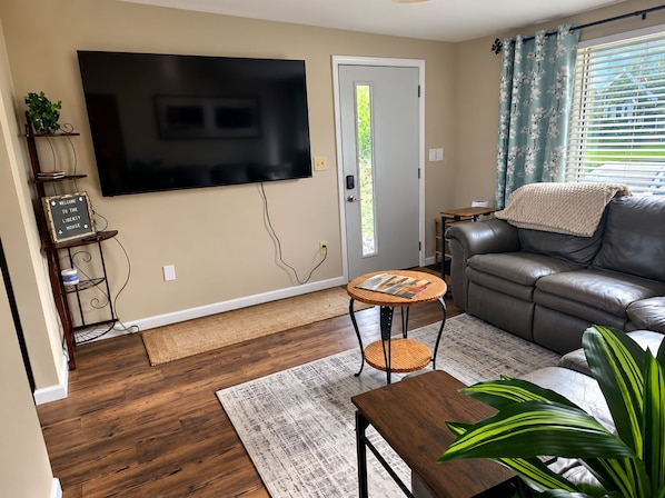 A living room with a flat-screen TV, a sofa, a coffee table, and a door with a window. - The Liberty House / 3 BR • 2 BA / SPIRE • Wineries • Lake Erie (Geneva)
