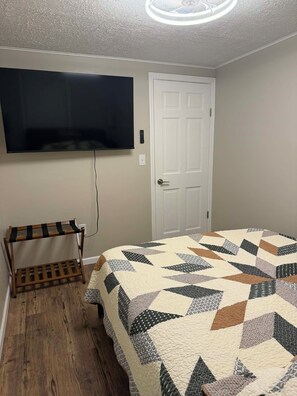 A bedroom with a bed, a television mounted on the wall, a door, and a wooden bench. - The Liberty House / 3 BR • 2 BA / SPIRE • Wineries • Lake Erie (Geneva)