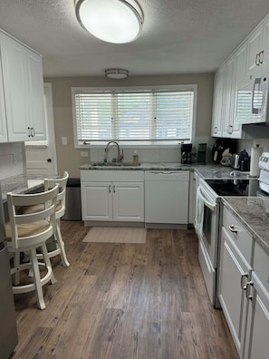 A kitchen with white cabinets, a built-in oven, a sink, and a window with blinds. - The Liberty House / 3 BR • 2 BA / SPIRE • Wineries • Lake Erie (Geneva)