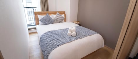 A neatly made bed with a striped blanket, pillows, and rolled towels.