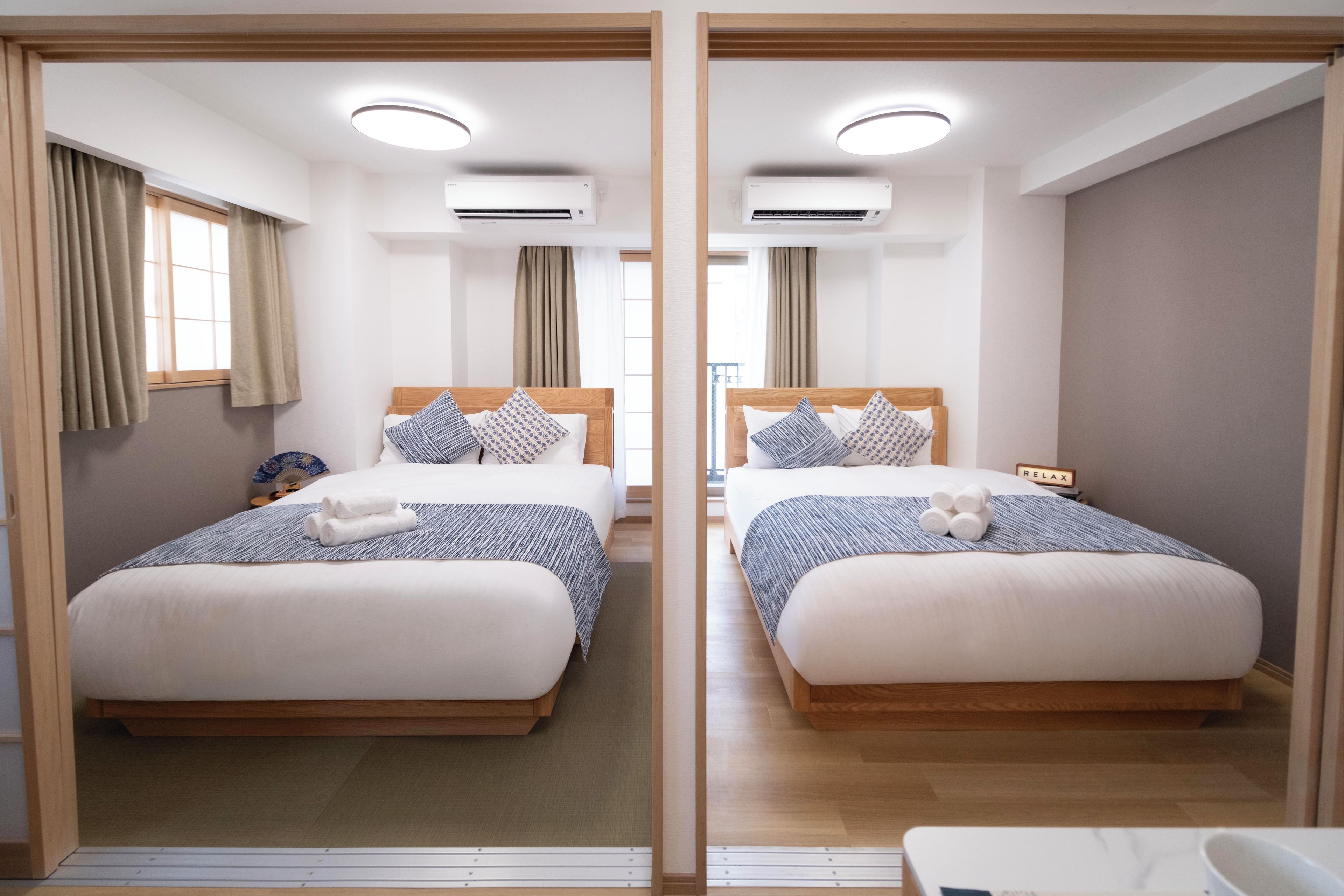 A mirrored room with two beds, each with a wooden headboard, white bedding, and a blue and white striped blanket.