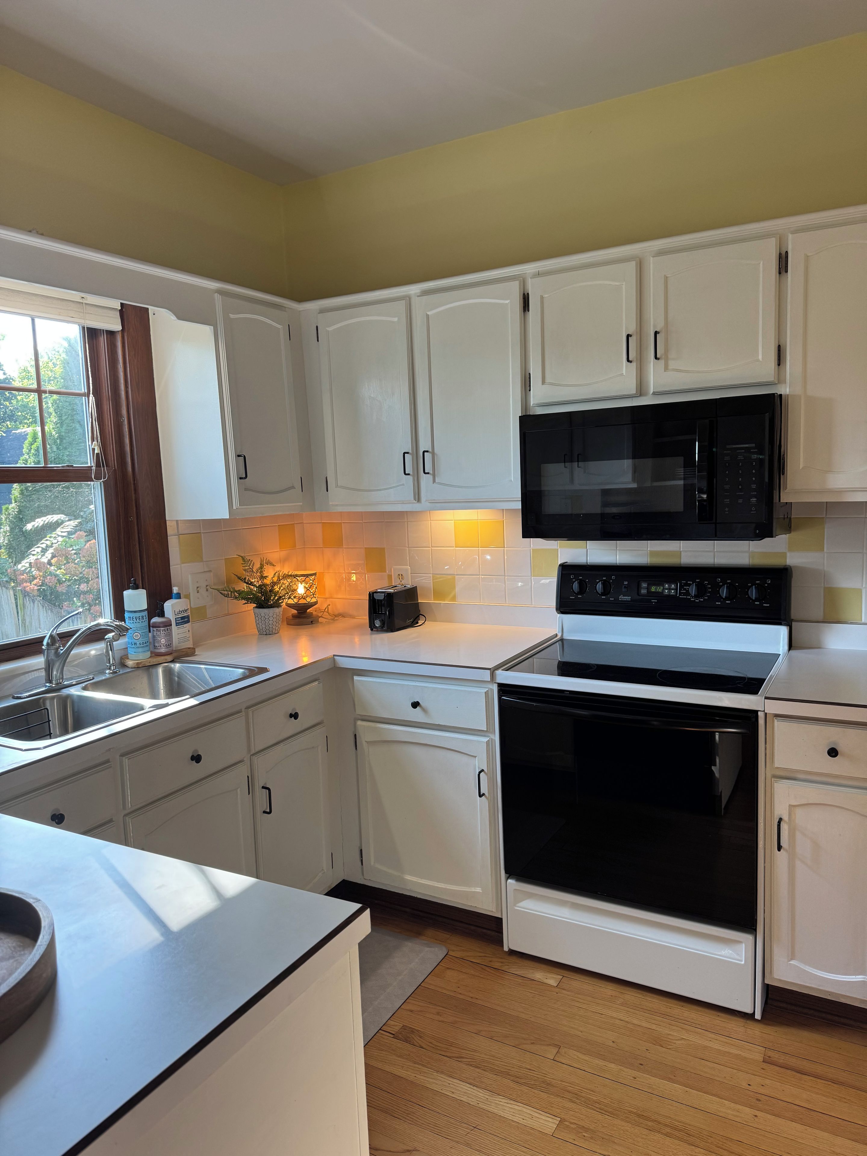 A kitchen with white cabinets, a microwave, an oven, and a sink.