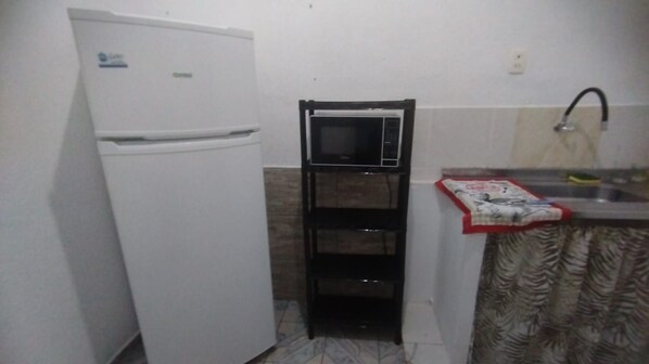 A compact kitchen with a white refrigerator, a black microwave, and a sink with a faucet.
