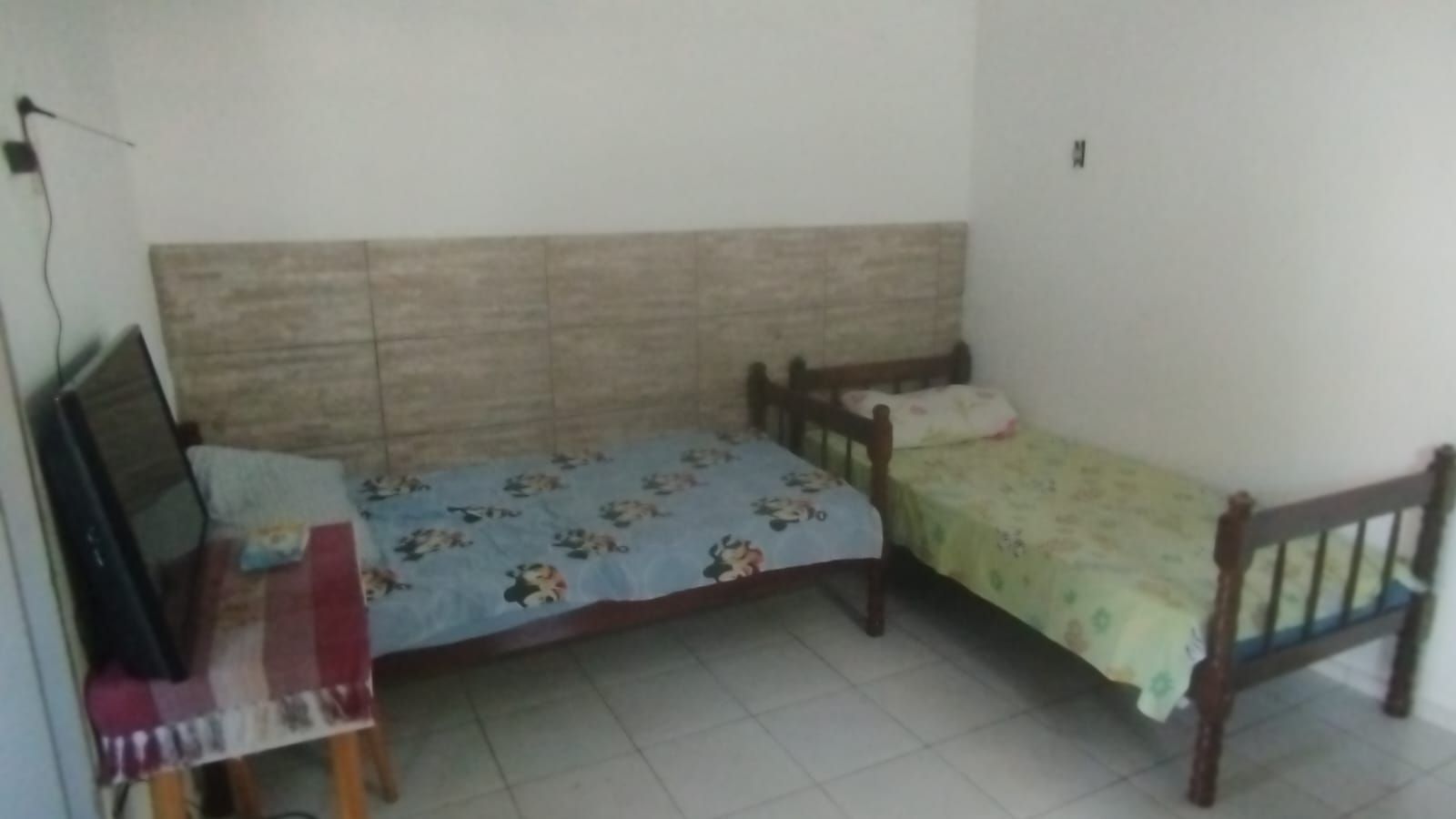A small room with two single beds, a wooden headboard, a desk with a chair, and a television.