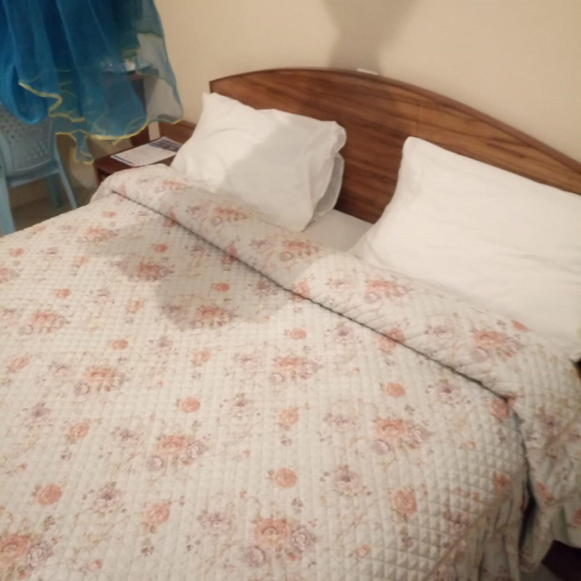 A bed with a floral-patterned bedspread and two pillows. - Blue Bay Hotel (Nakuru)