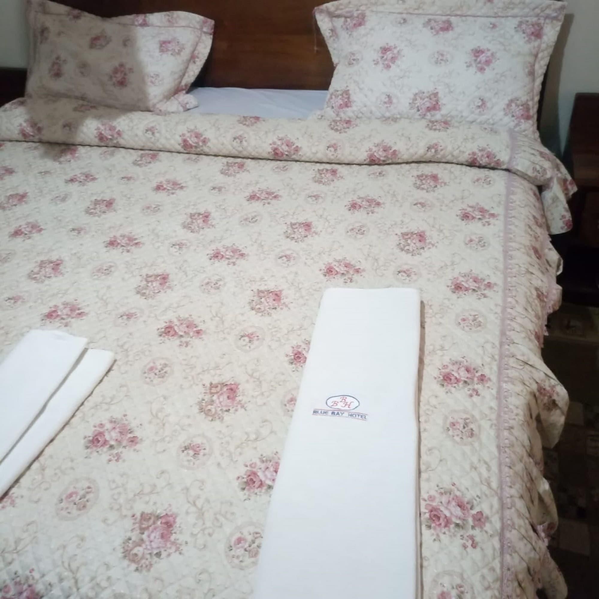 Una cama con colcha de estampado floral, almohadas y una toalla blanca doblada cuidadosamente.