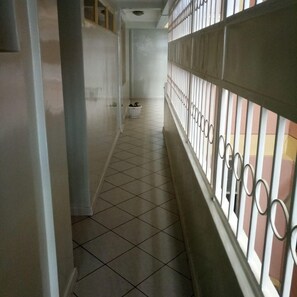 A corridor with tiled flooring, a white wall, and a metal railing on one side. - Blue Bay Hotel (Nakuru)