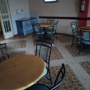 A dining area with round tables and chairs, a blue cabinet, and a tiled floor. - Blue Bay Hotel (Nakuru)