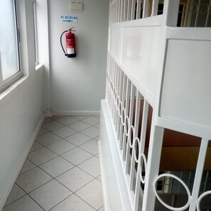 A corridor with a tiled floor, a fire extinguisher mounted on the wall, and a sign indicating directions. - Blue Bay Hotel (Nakuru)