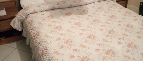 A bed with a floral patterned bedspread, two white pillows, and a blue curtain.