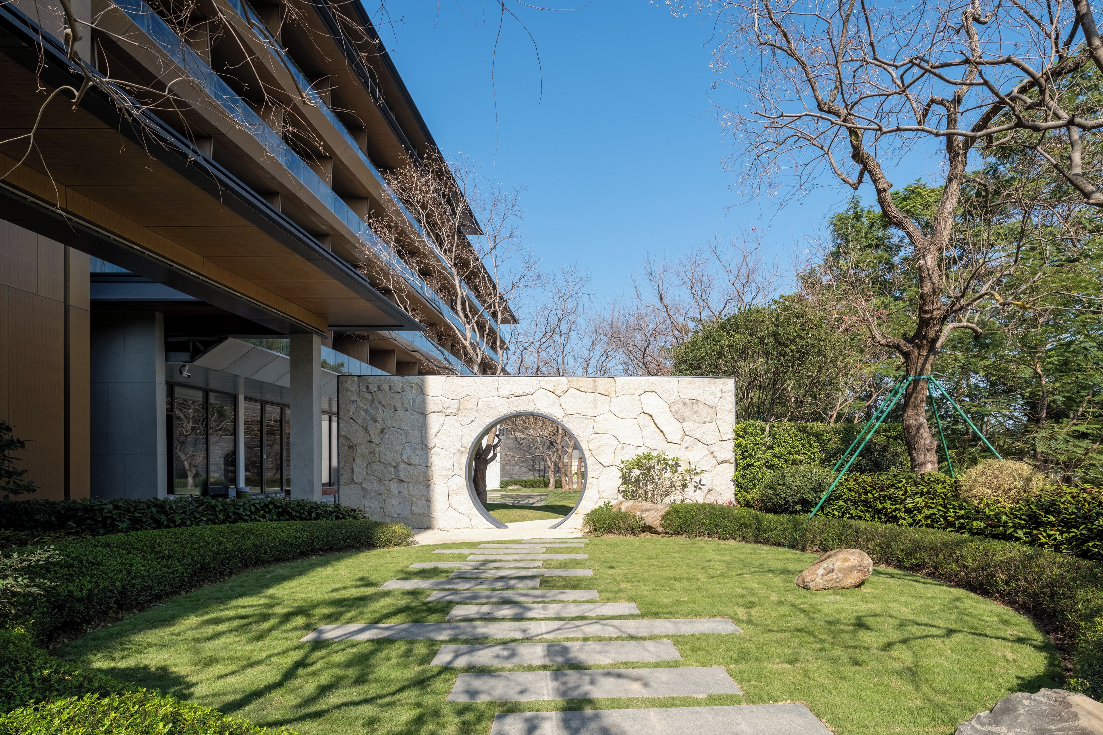 Un edificio moderno con un arco de piedra, un césped cuidado y un cielo despejado.