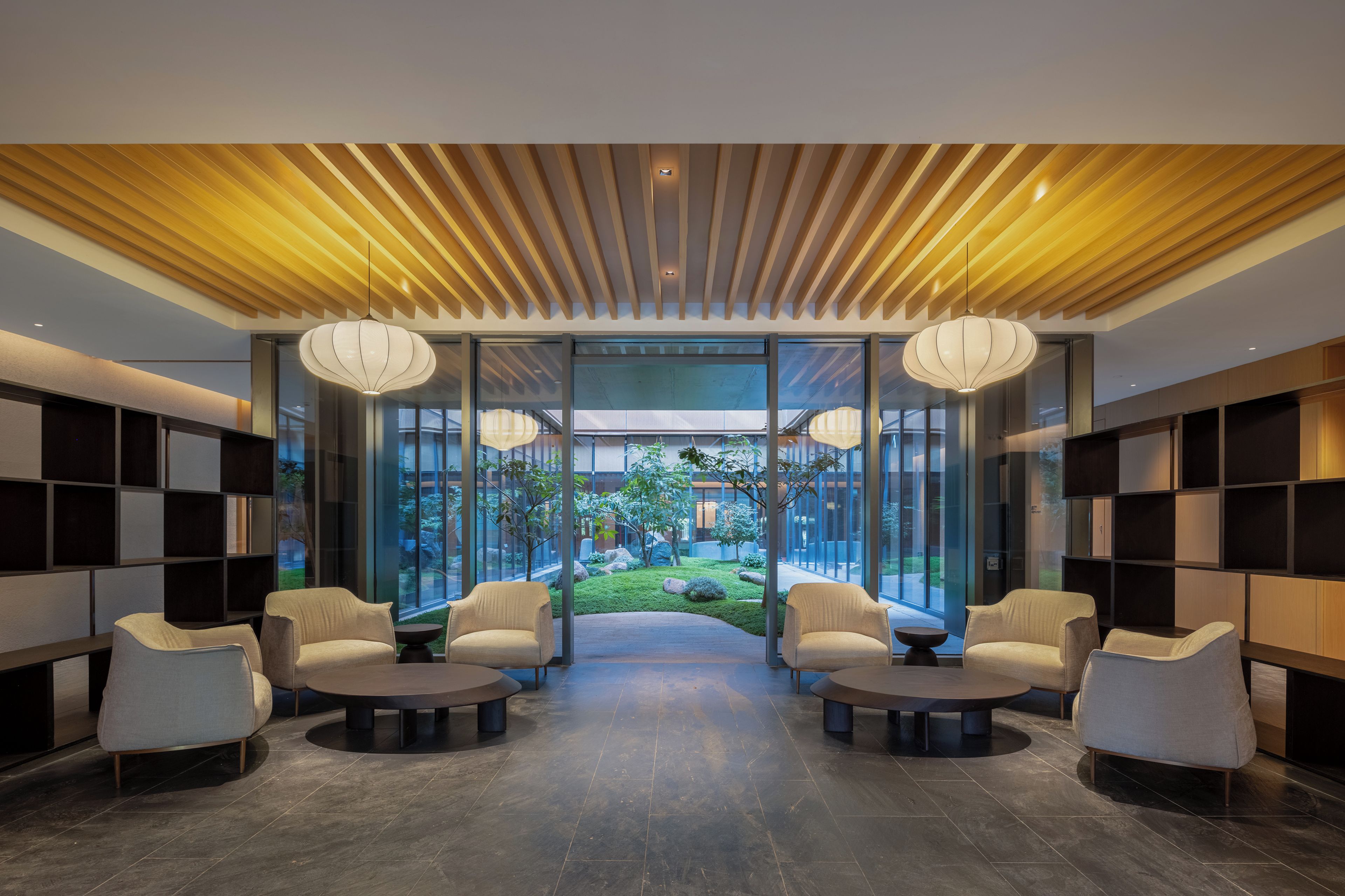 A modern lobby with a central seating area, glass walls, and a view of a garden.