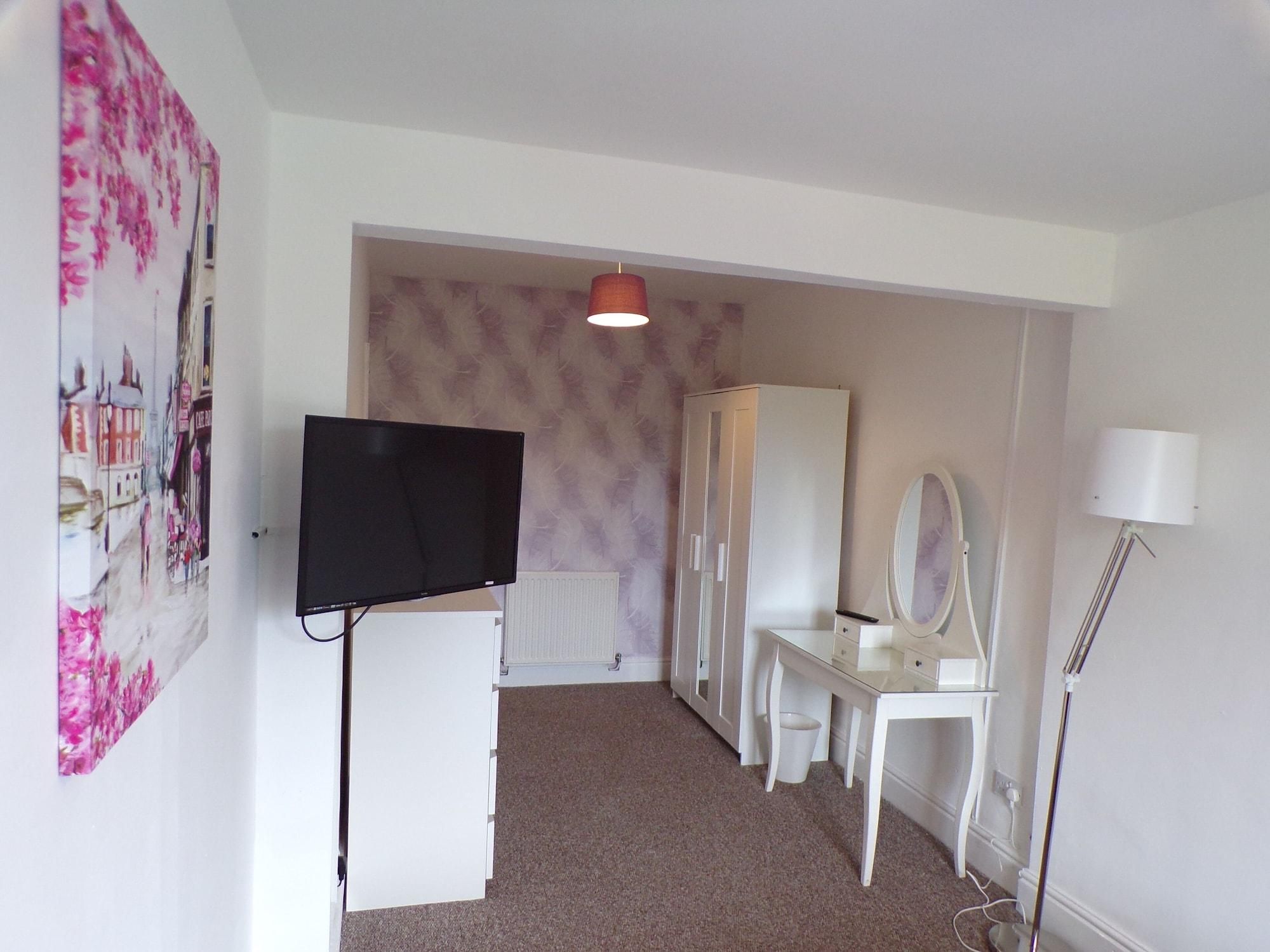 Una habitación con televisor, armario, tocador con espejo y lámpara.