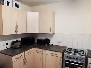 A kitchen with light wooden cabinets, a gas stove, a toaster, and a slow cooker.