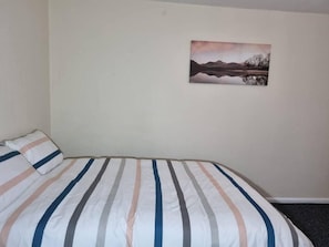 A single-bed room with a striped bedspread, a pillow, and a wall-mounted picture of a landscape.