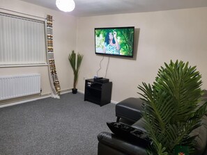 A living room with a television mounted on the wall, a black leather sofa, a potted plant, and a radiator.