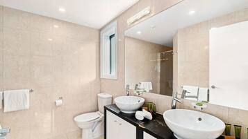 A modern bathroom with a large mirror, two sinks, a toilet, and a shower.