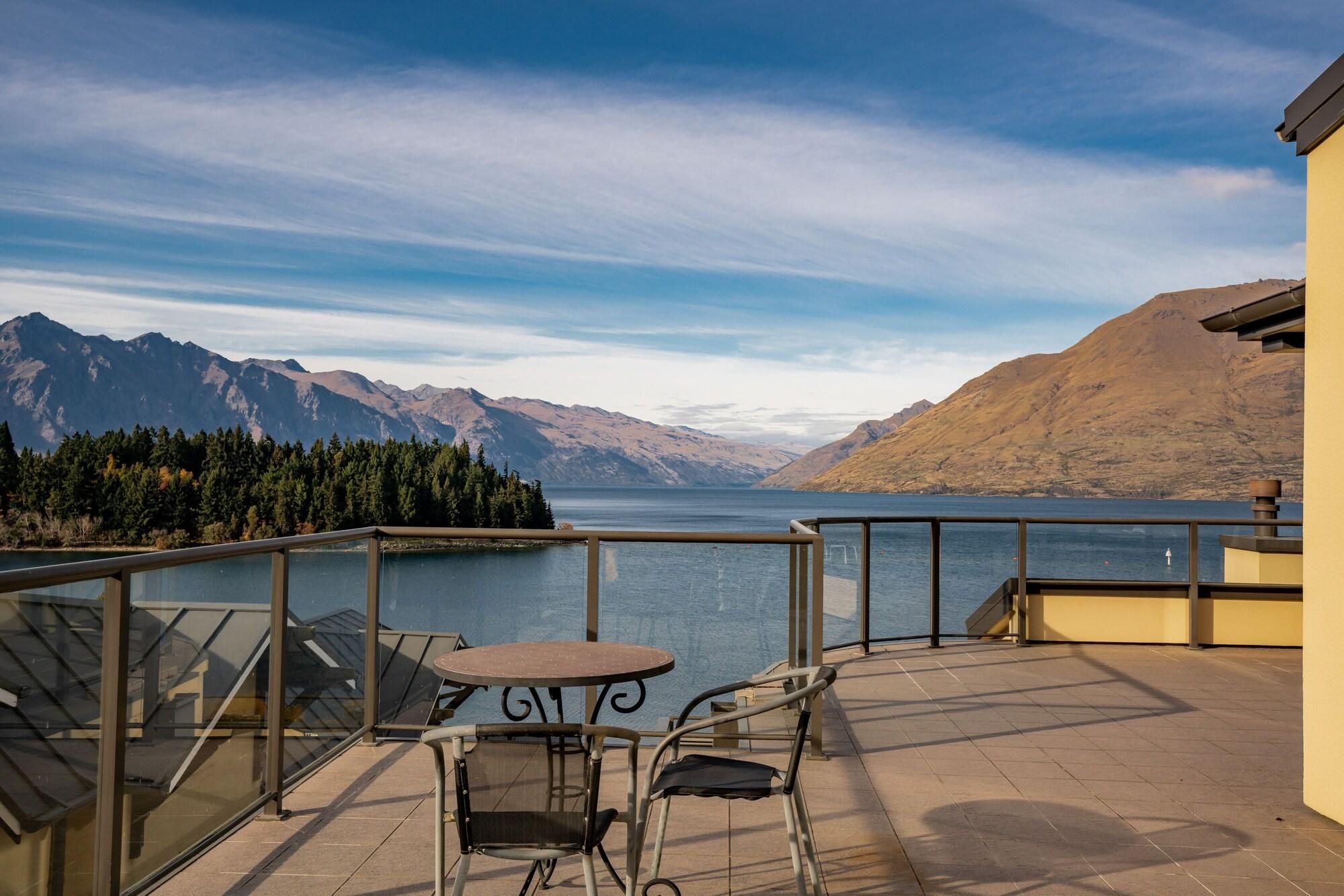 Una terrazza con tavolo e sedie che si affaccia su un lago e montagne.