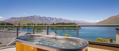 A hot tub on a balcony overlooking a lake with mountains in the background.