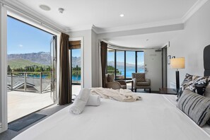 Ein Hotelzimmer mit einem großen Bett, einer Sitzecke mit Blick auf einen See und Berge sowie einem Balkon mit einer Glastür.