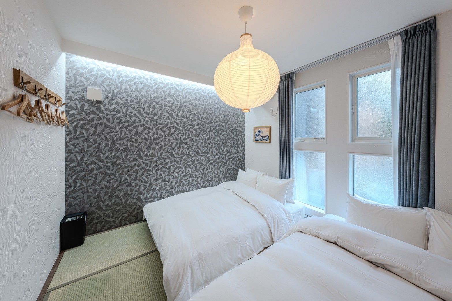 A hotel room with a bed, a hanging light fixture, a window with curtains, and a wall with a leaf pattern.