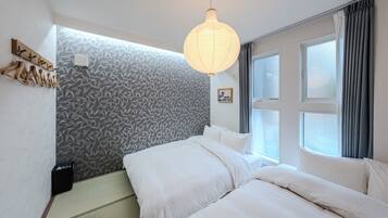 A hotel room with a bed, a hanging light fixture, a window with curtains, and a wall with a leaf pattern.