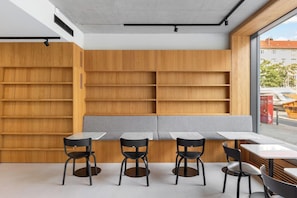 A modern interior with a long wooden bookshelf, a bench, and four tables with chairs. - Stilwerk Hotel Kantgaragen (Berlin)