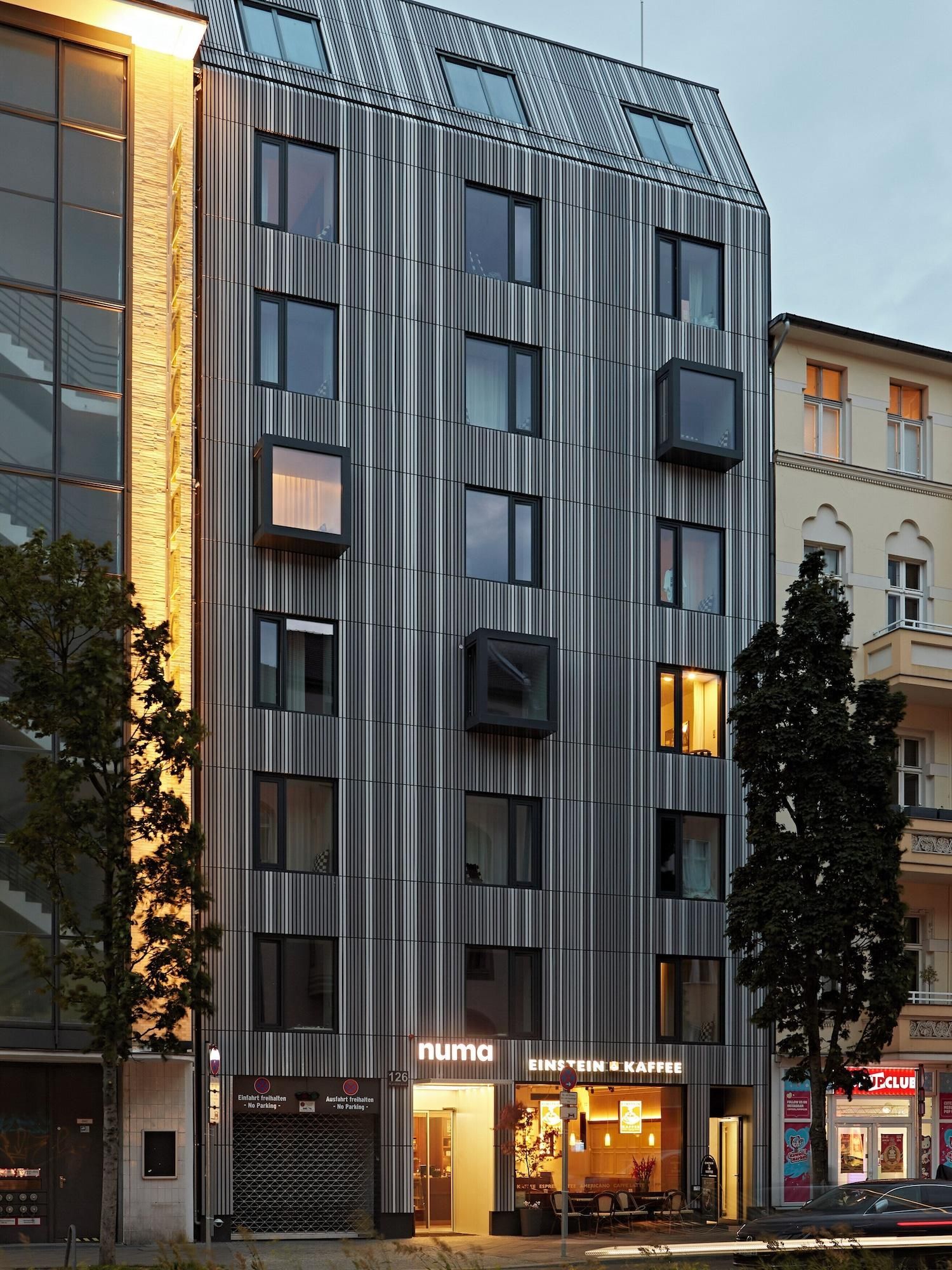 A modern building with a vertical striped facade, a ground-level entrance, and a visible coffee shop named 'EINSTEIN & KAFFEE' with outdoor seating.