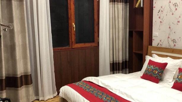 A hotel room with a wooden bed, white bedding, a red throw, a wooden desk, and a window with curtains. - Li Sen Hotel Resort (Enshi)