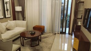 A hotel room with a sofa, a coffee table, a small ottoman, a lamp, and a television. - Li Sen Hotel Resort (Enshi)