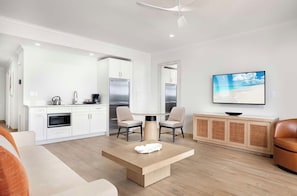 A modern kitchen with white cabinetry, a dining table with chairs, a television on the wall, and a sofa in the living area.