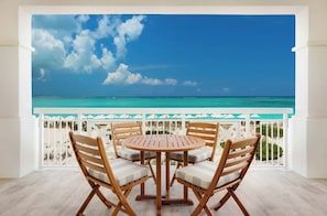 Un balcon avec vue sur l’océan, des chaises en bois et une balustrade blanche.