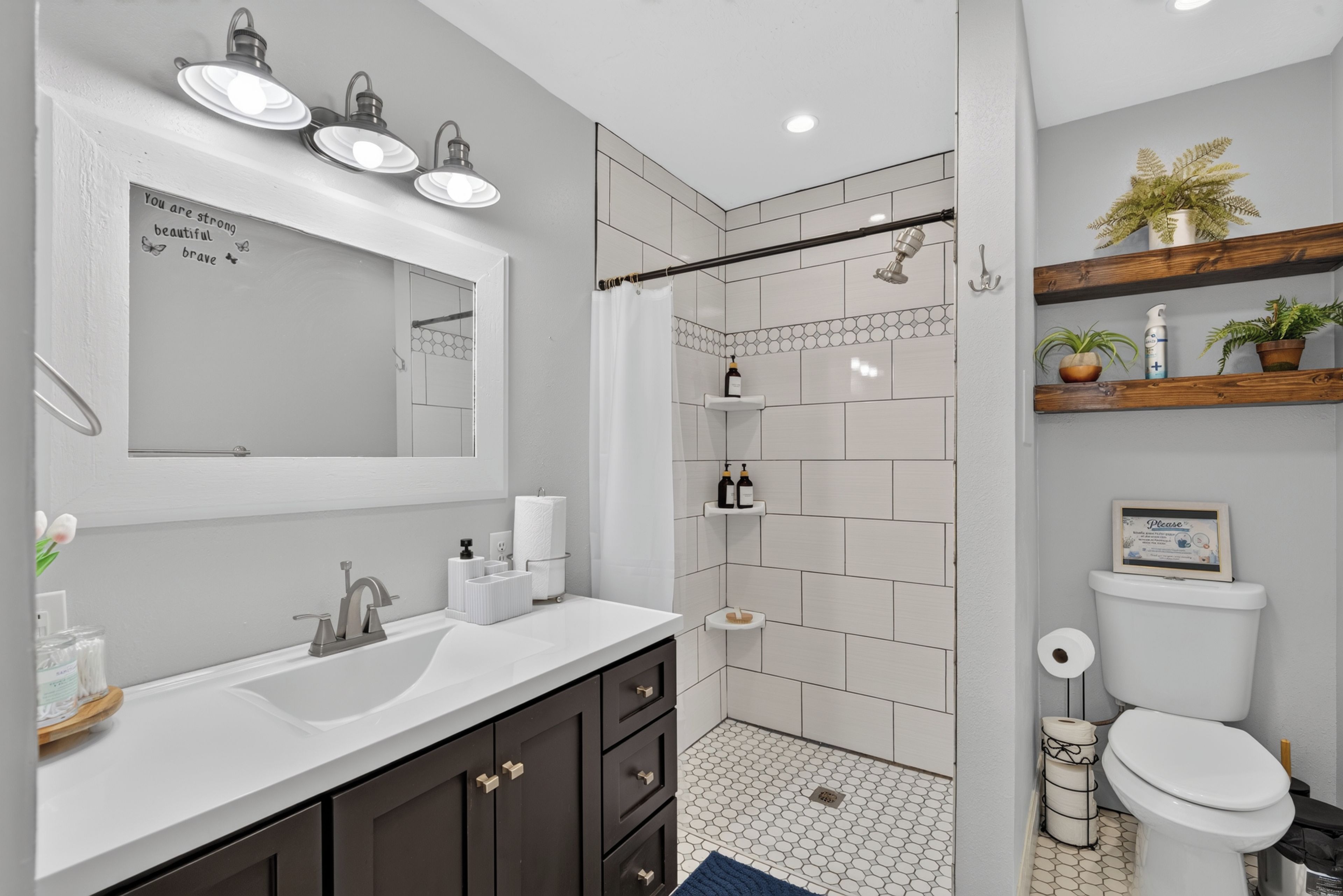 A modern bathroom with a large mirror, a sink, a shower, and a toilet.