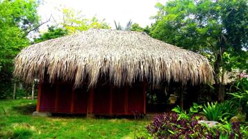 A thatched-roof structure with a red wall, surrounded by greenery.